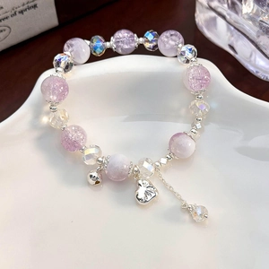 Macro shot of purple beaded bracelet with heart pendant and bell on a ceramic tray