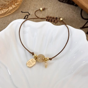 Detail of woven brown cord bracelet with Zhaocai charm and Citrine bead on a shell plate