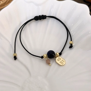 Close-up of woven bracelet with golden Zhaocai charm and beads on a shell plate