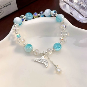 Detail of light blue beaded bracelet with sparkling silver fishtail charm on white plate