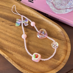 Detailed shot of pink beaded phone charm with bow and strawberry charms on wooden tray