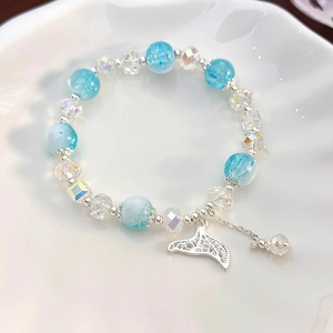 Macro detail of blue crystal bead bracelet with silver whale tail charm in shell plate