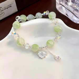 Detail of beaded mint green crystal bracelet with heart pendant on white ceramic plate