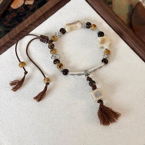 Dettaglio del bracciale con perline a stella in ceramica, occhio di tigre e cordino intrecciato