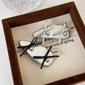 Silver ballet style leather bow hair clips set with metallic beads on beige background
