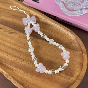 Detail of pink bow and pearl beaded phone strap on an elegant wooden tray display