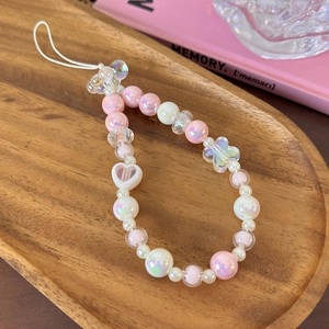 Detailed view of pink beaded phone strap with iridescent heart and flower beads on wood