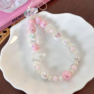 Detailed view of pink beaded phone charm with heart and cloud accents in ceramic tray