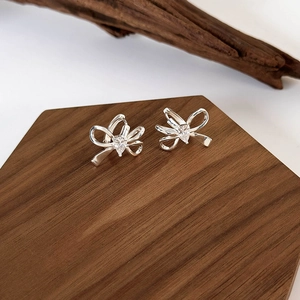 Dettaglio orecchini a fiocco in argento con zircone su supporto in legno