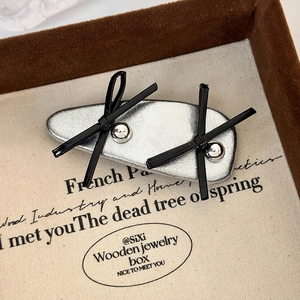Detail of silver leather bow hair clip with black ribbons and metallic studs in a vintage box