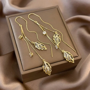 Elegant gold leaf earrings with white cat eye stones and long tassels on jewelry box