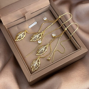Detail view of gold leaf drop earrings with white cat eye stone and zircon tassels