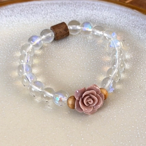 Detail of beaded bracelet with iridescent clear beads and a pink resin rose charm