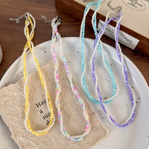 Colorful beaded pearl necklaces in yellow, blue, and purple set on a white ceramic plate