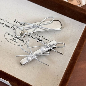 Silver bow hair clips with pearls and heart pendants on a wooden jewelry display