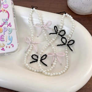 Handmade pearl phone charm with cute beaded bows on a minimalist ceramic display