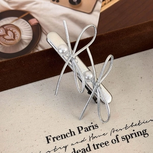 Detailed view of elegant silver bow hair clip with white pearls on a stylish fabric background