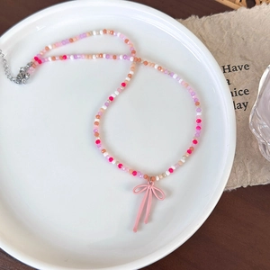 Detail van kleurrijke glazen kralenketting met roze strikhanger op een wit bord
