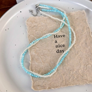 Detail of double-layer beaded necklace with white pearls and light blue beads and silver clasp
