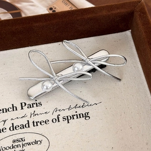 Detail of silver bow hair clip featuring double pearls and intricate woven metallic texture