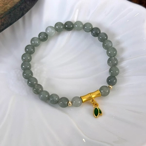 Détail du bracelet en jade vert avec motif bambou et breloques feuilles sur plat en céramique