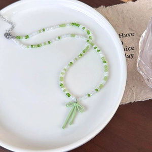 Detailopname van groen-witte glazen kralenketting met matte strikhanger op bordje
