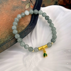 Détail de bracelet en perles de jade avec nœud de bambou doré et breloque feuille