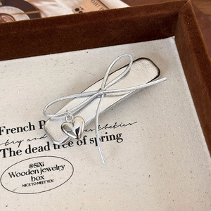 Close-up of silver bow hair clip with heart pendant on a beige canvas display tray