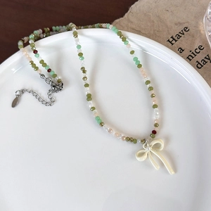 Detail van kleurrijke kralenketting met crème strikhanger en parel op wit bord