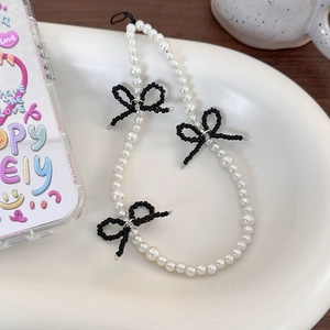 Detail of beaded phone strap with white pearls and black bows on a cream tray