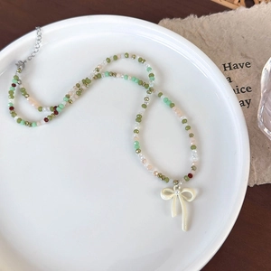 Detailopname van kleurrijke glazen kralenketting met een witte strik hanger in schaal
