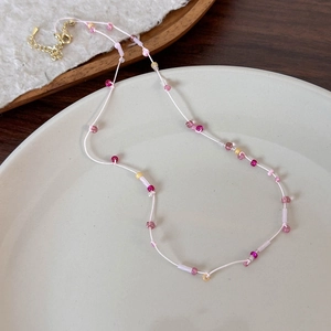 Dettaglio della collana di perline colorate con stelle e fiori su piatto bianco e chiusura