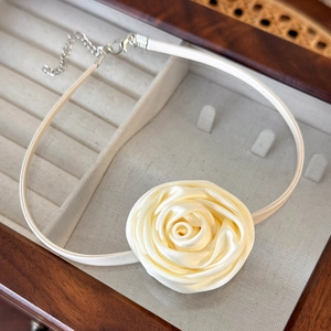 Detail shot of a beige satin fabric rose choker with an adjustable silver metal clasp