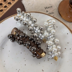 Three elegant hair claws with pearls and metallic beads displayed on a stylish ceramic plate