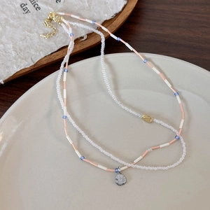 Dettaglio di una collana a due strati con perline, pendente a margherita e chiusura oro