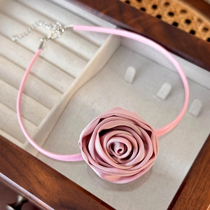 Detail of pink satin rose choker with leather band on a luxury wooden jewelry box