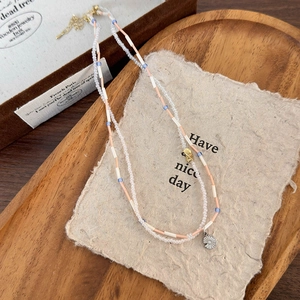 Dettaglio collana di perline con tubi arancioni, perle blu e ciondolo a girasole su legno
