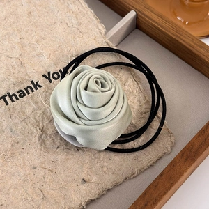 Detailed close-up of mint green satin rose scrunchie with elastic hair tie on a tray