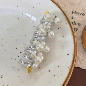 Detailed macro view of a clear spiral hair tie with pearls and gold ends on a ceramic plate