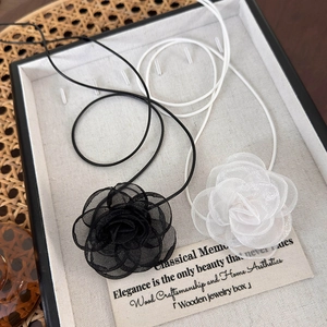 Détail des colliers camélia en organza multicouches noir et blanc sur un plateau rétro
