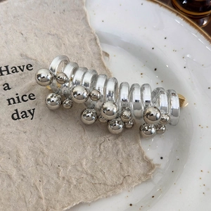Macro shot of silver metallic spheres and clear spiral tube on a minimalist ceramic plate