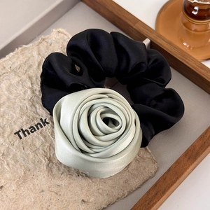 Detail of mint green satin rose hair scrunchie with black fabric on wooden tray