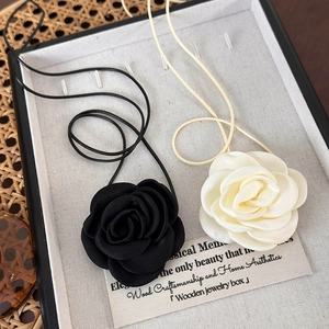 Détail de colliers camélia noir et crème présentés sur un support vintage tissé