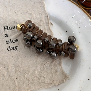 Detailed view of brown spiral hair coil with grey beads on a textured paper background