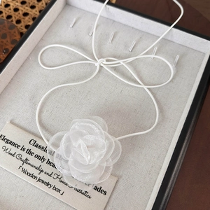 Détail d'un choker camélia en organza blanc dans un coffret à bijoux en bois