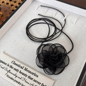 Vue détaillée du collier choker rose en maille noire sur un présentoir blanc texturé