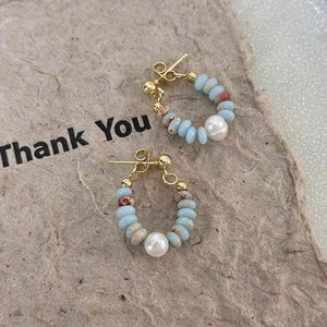 Detail of beaded hoop earrings with light blue stone beads and a white pearl accent