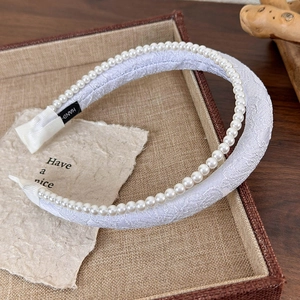 Detail view of handmade white lace headband with elegant pearls and interior label
