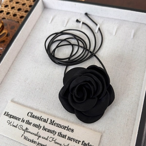 Détail d'un collier choker rose en tissu noir avec de longs cordons en satin ajustables