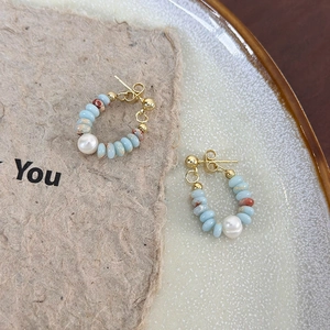 Detail of C-shaped earrings with sky blue stones, brown beads, and white freshwater pearls